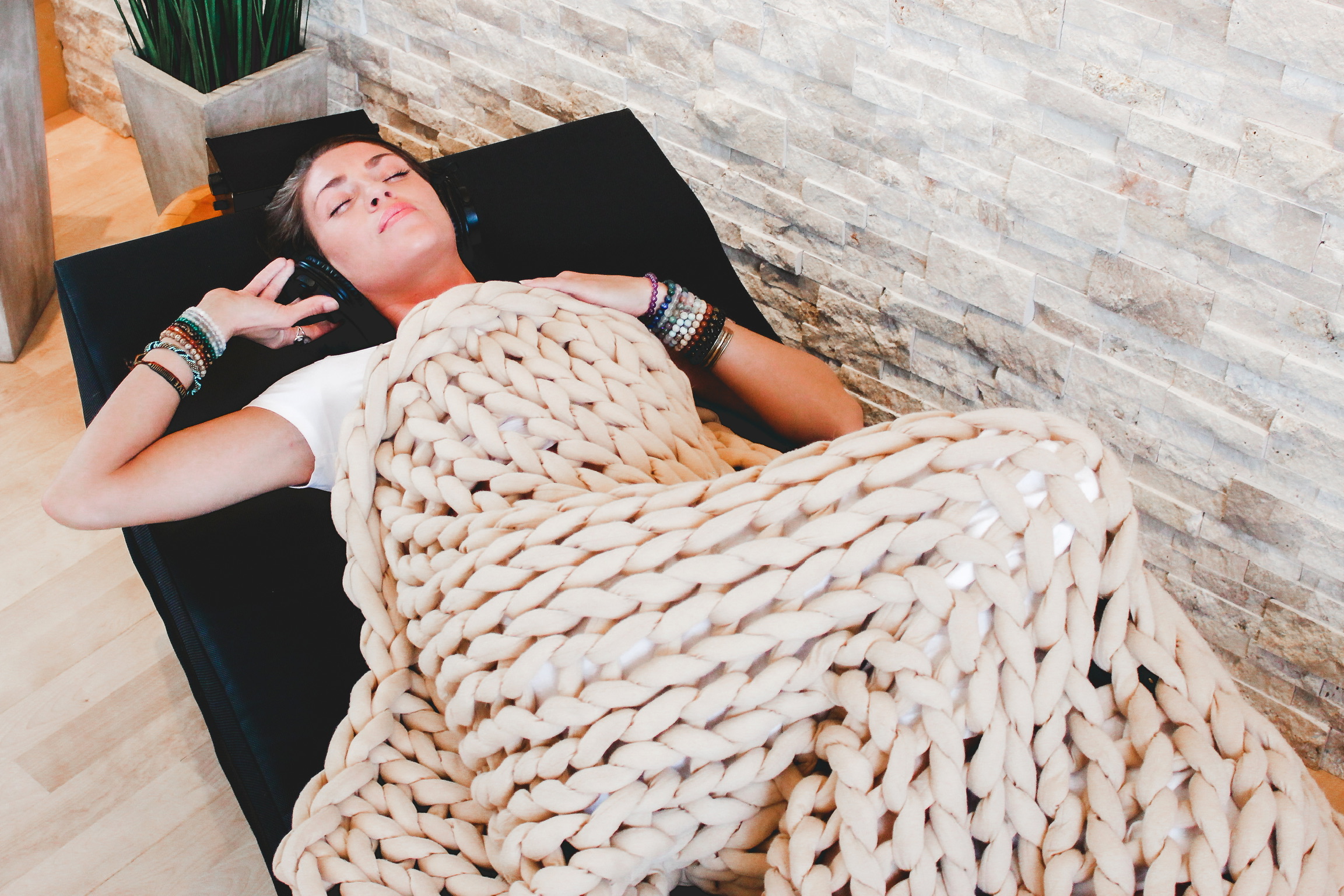 Person relaxing under a chunky knit blanket in a VibroAcoustic lounge chair with headphones, experiencing sound therapy alongside safe psilocybin treatment in Oregon