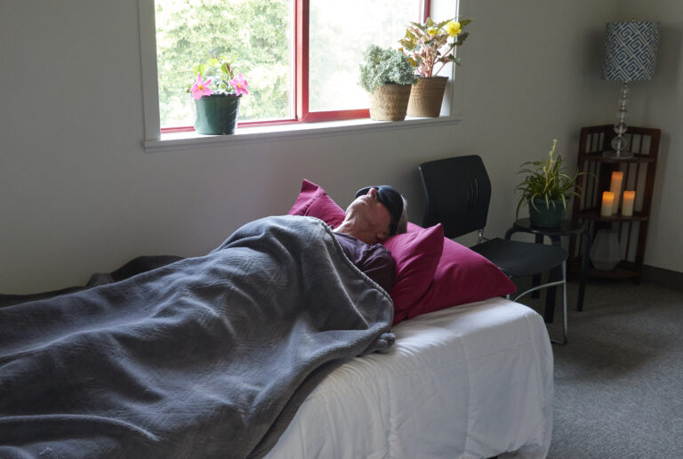 Older adult reclining under a blanket in a psilocybin session room in Oregon, immersed in a quiet healing experience.