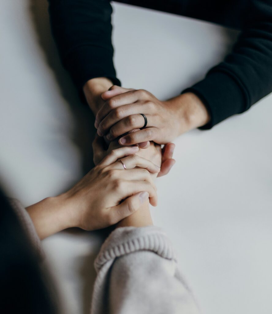 Two people holding hands at a table, symbolizing support, connection, and healing during a psilocybin experience in Oregon.