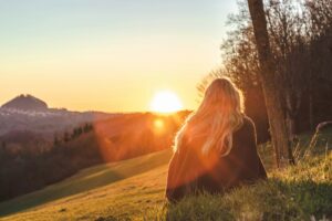 Woman sitting alone in a grassy field at sunset, reflecting and finding peace after a challenging psilocybin experience in Oregon