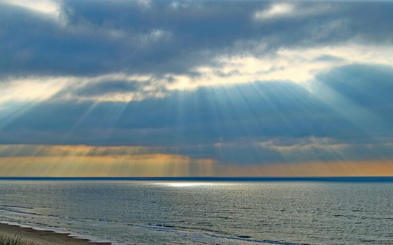 Sunlight breaking through clouds over the ocean, symbolizing spiritual clarity and awakening through psilocybin experiences in Oregon.